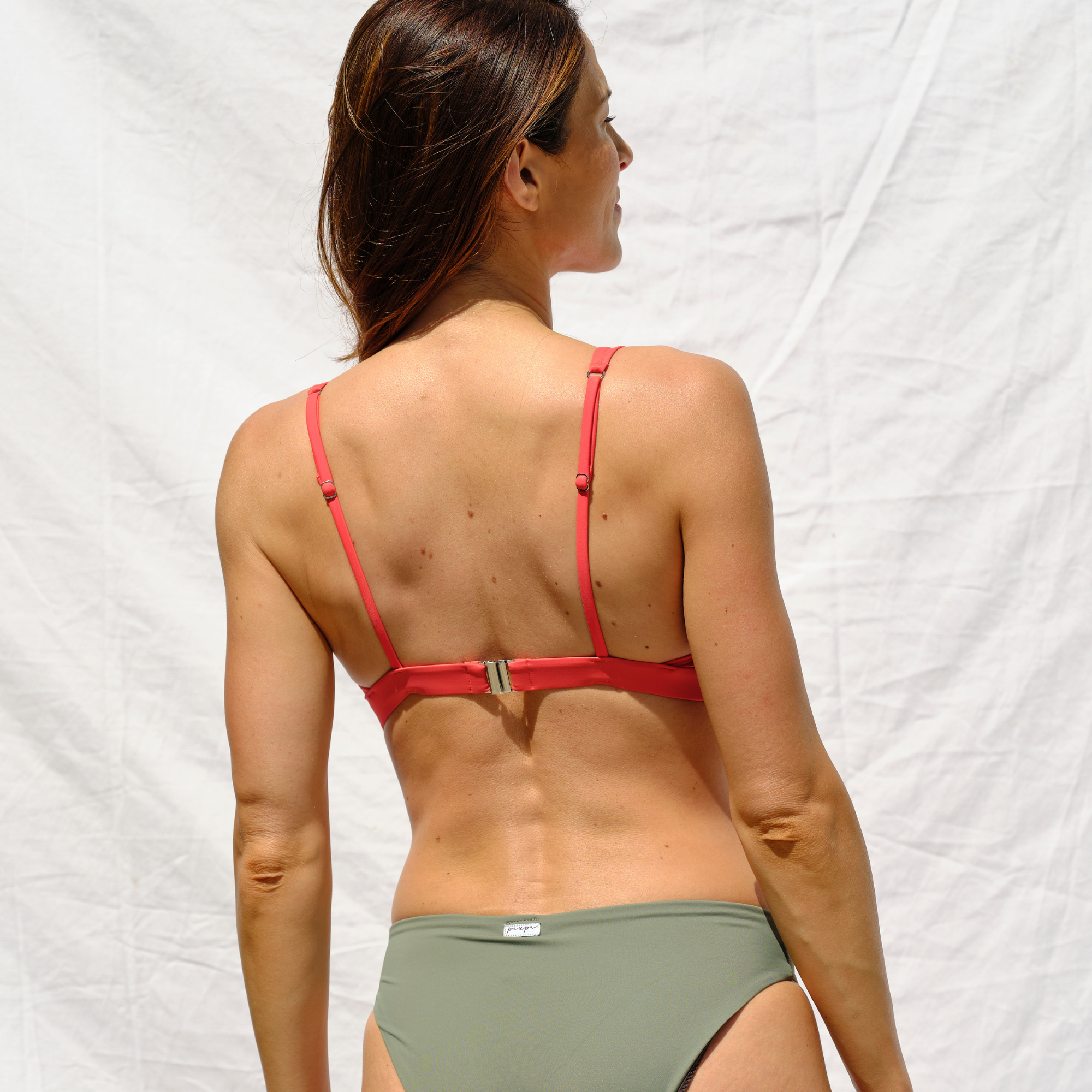 Woman wearing a red bikini top and khaki bottom by Paupa, back view