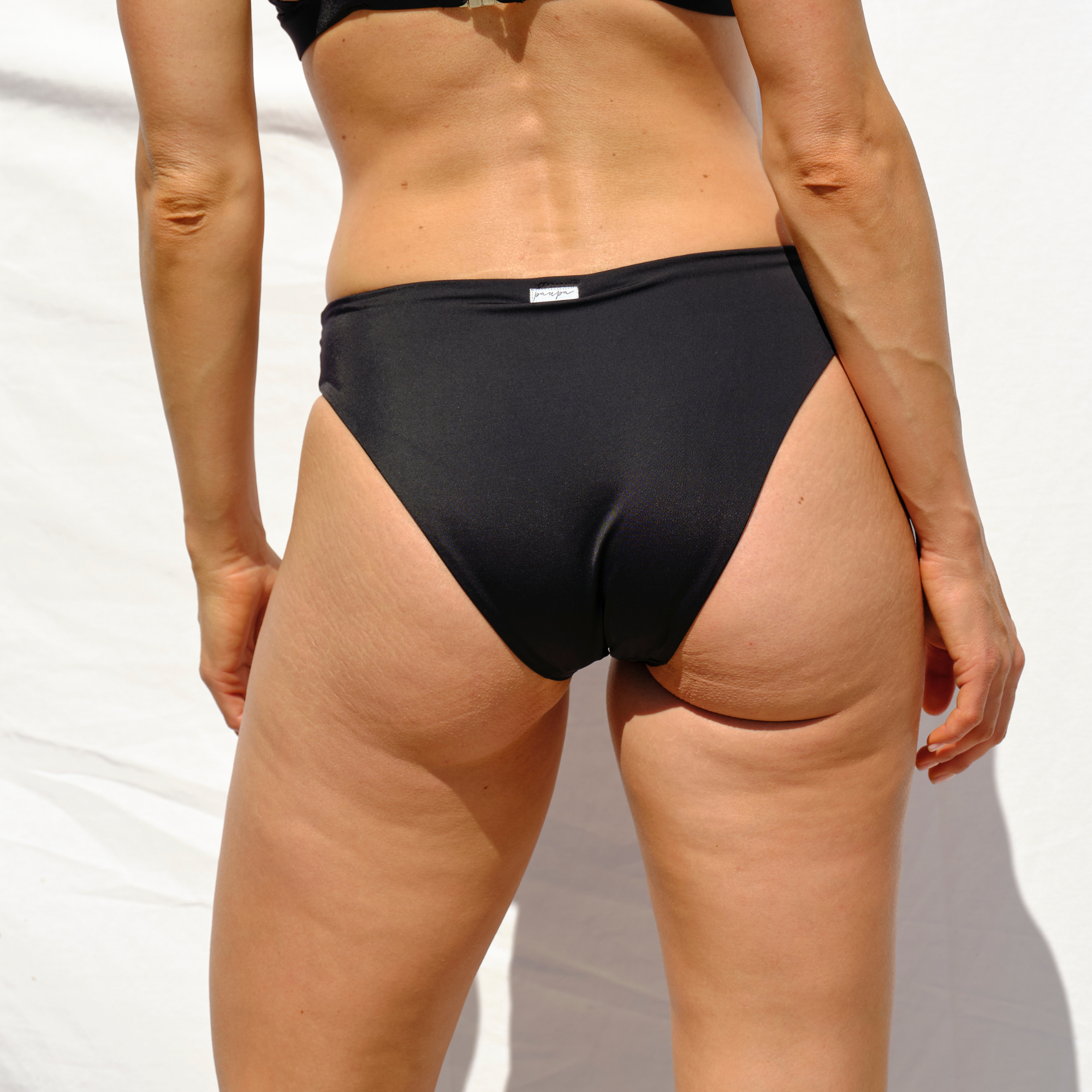 Woman wearing a black low-rise bikini bottom by Paupa, back view